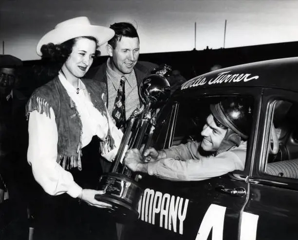  Curtis Turner accepts the winning trophey from Bill France Sr. and an unidentified woman after half the cars in Grand National had issue