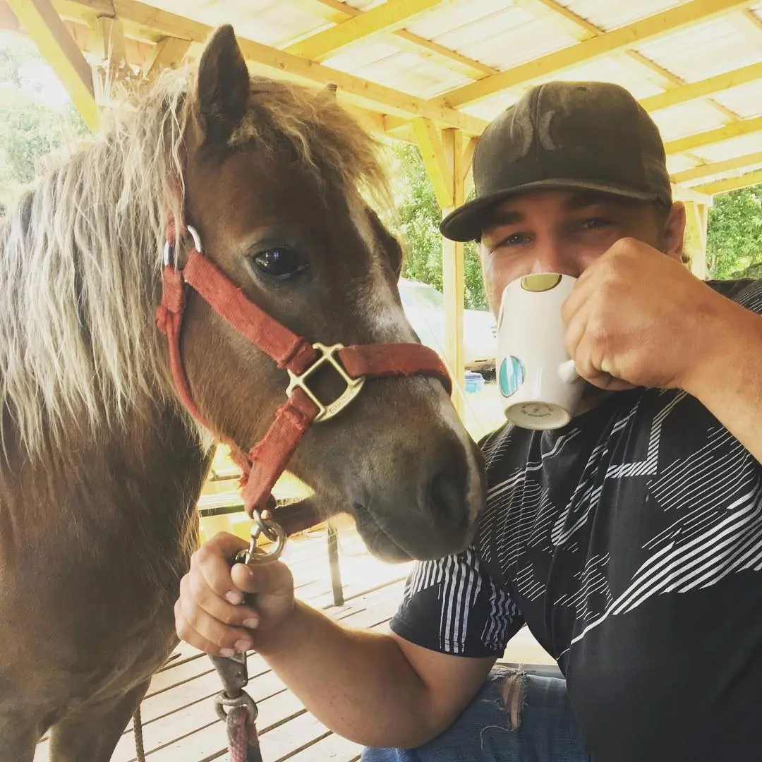 Matt is pictured alongside an 18-year-old pony while he drinks coffee.